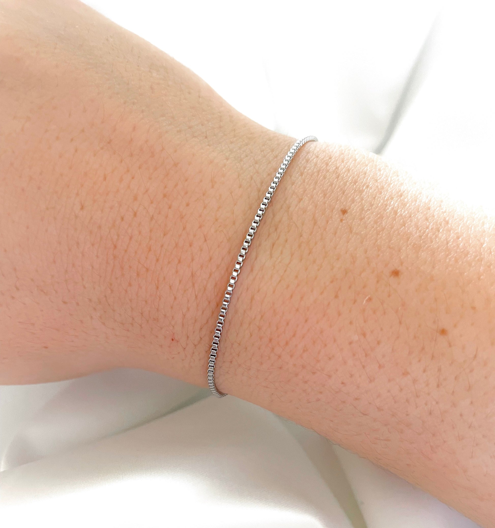 Top view of silver box chain bracelet on a person's wrist with a white background