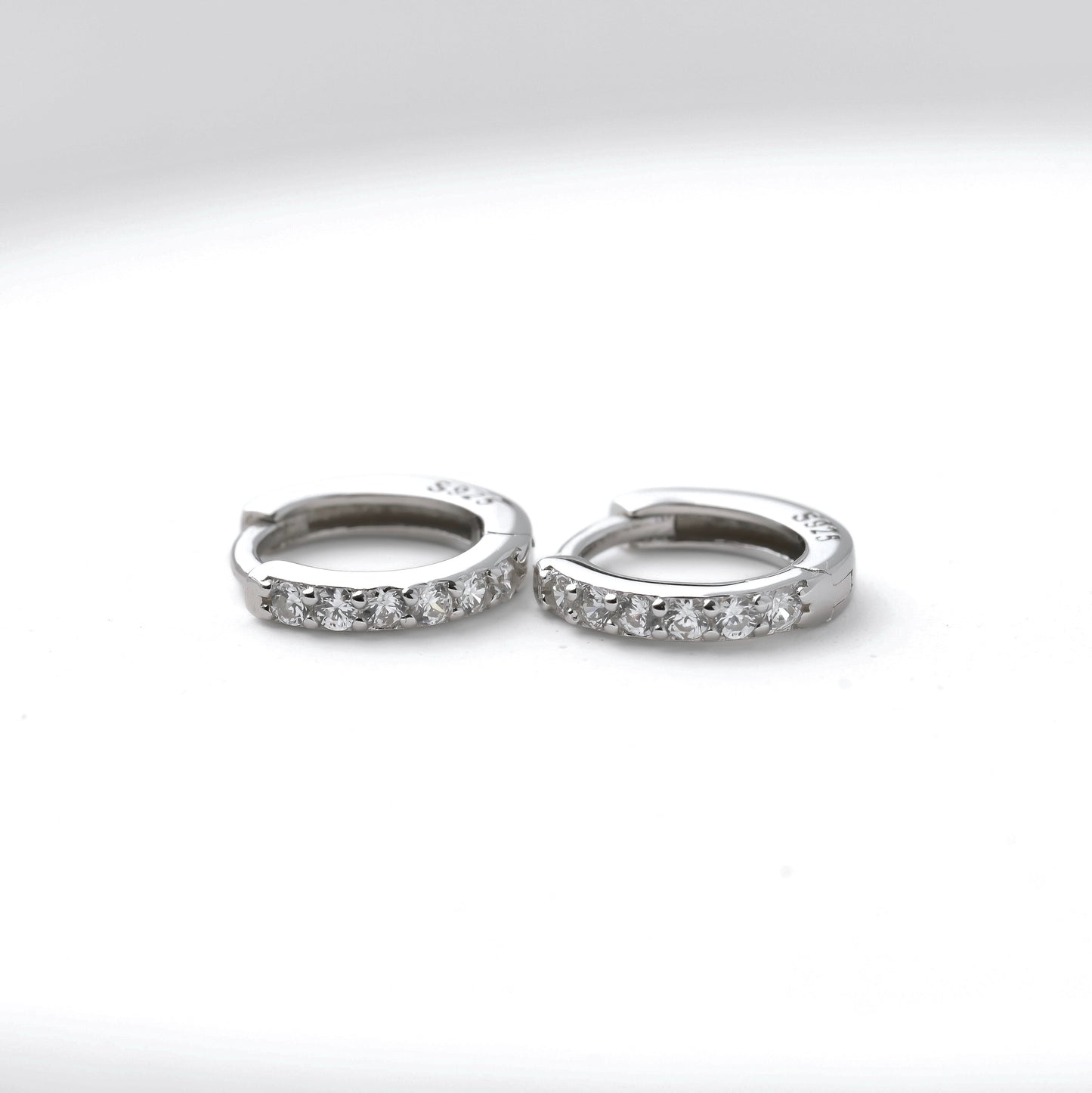 Pair of silver half eternity pave hoop earrings with S925 stamp on a white background