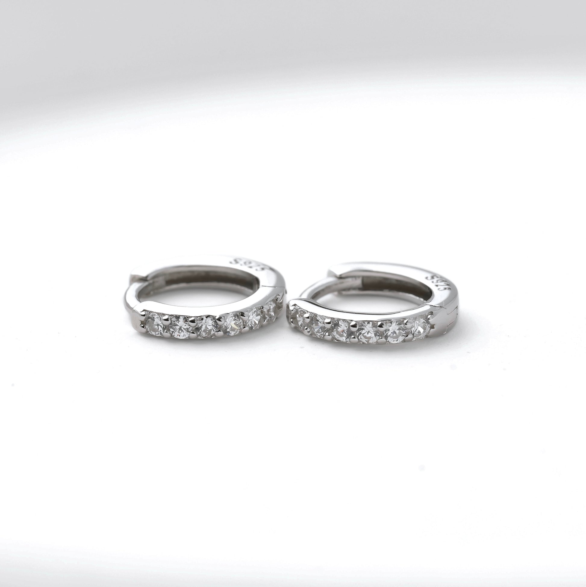 Pair of silver half eternity pave hoop earrings with S925 stamp on a white background