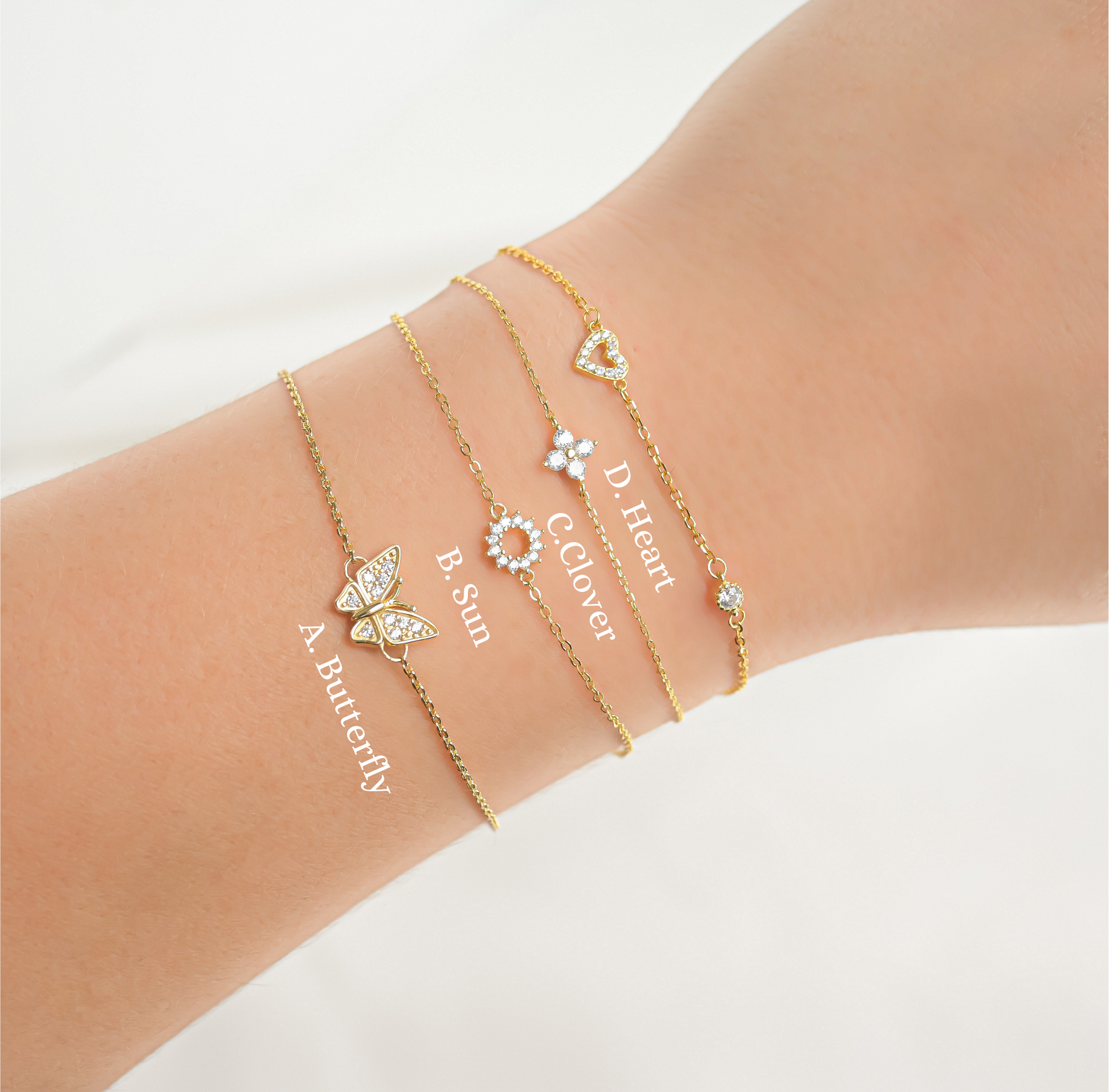 Gold bracelets with butterfly, sun, flower, and heart charms with the design labels on a wrist against a white background