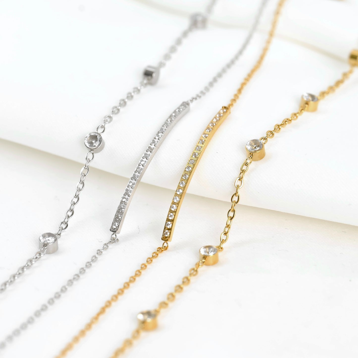 Four bracelets in gold and silver with bezel station and diamond bar designs on a light background