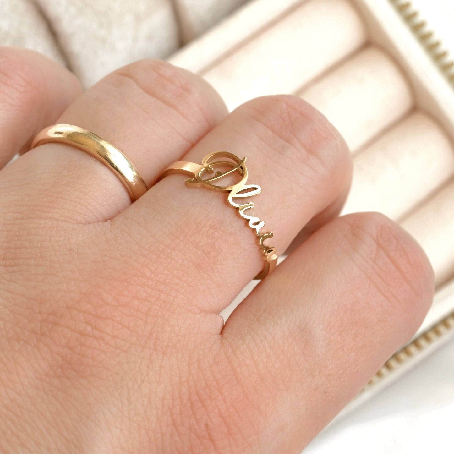Gold nameplate ring with 'Olivia' on a hand against a neutral background