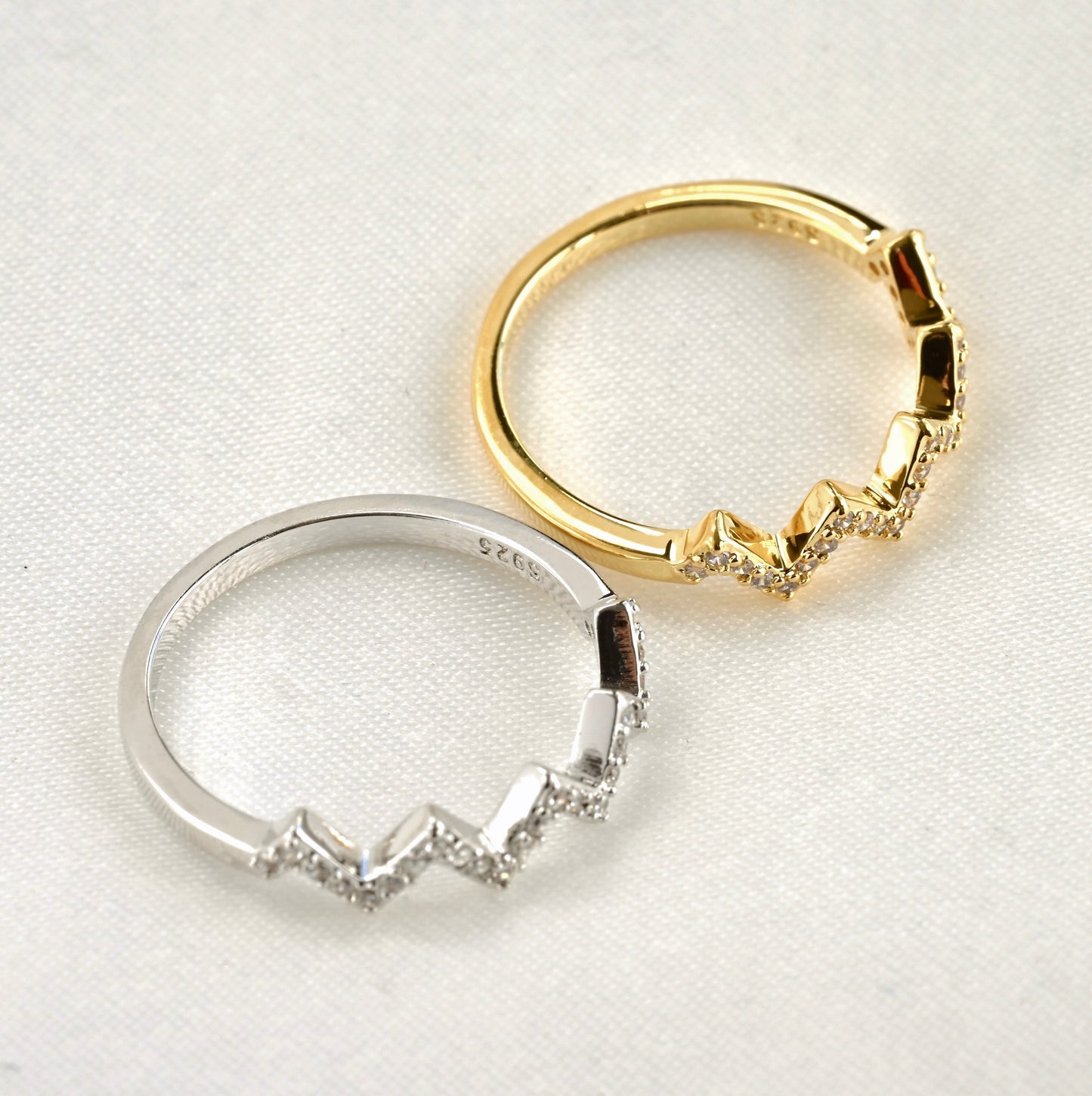 Top view of two zigzag gold and silver rings with S925 stamps with on a white background
