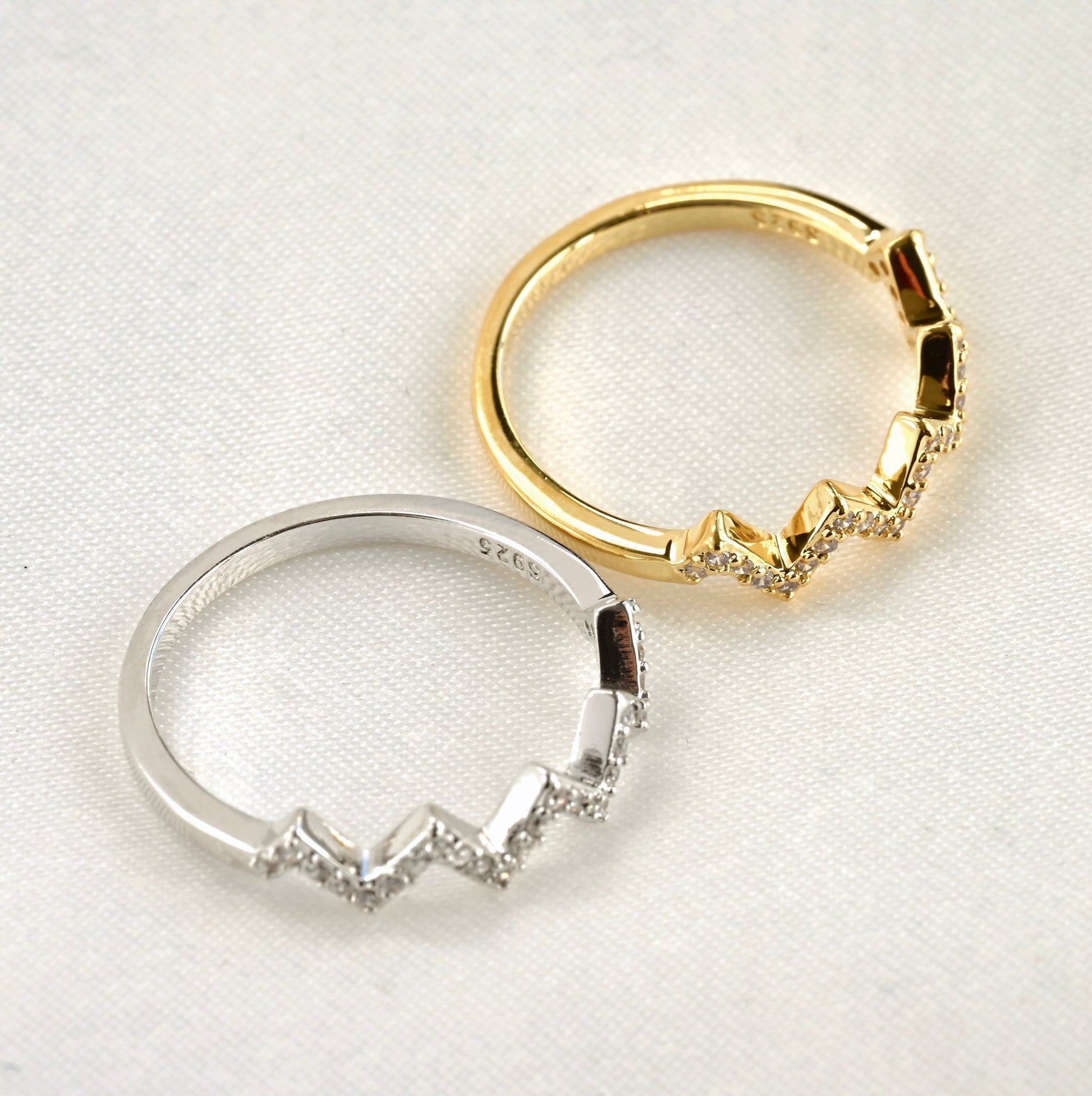 Top view of two zigzag gold and silver rings with S925 stamps with on a white background