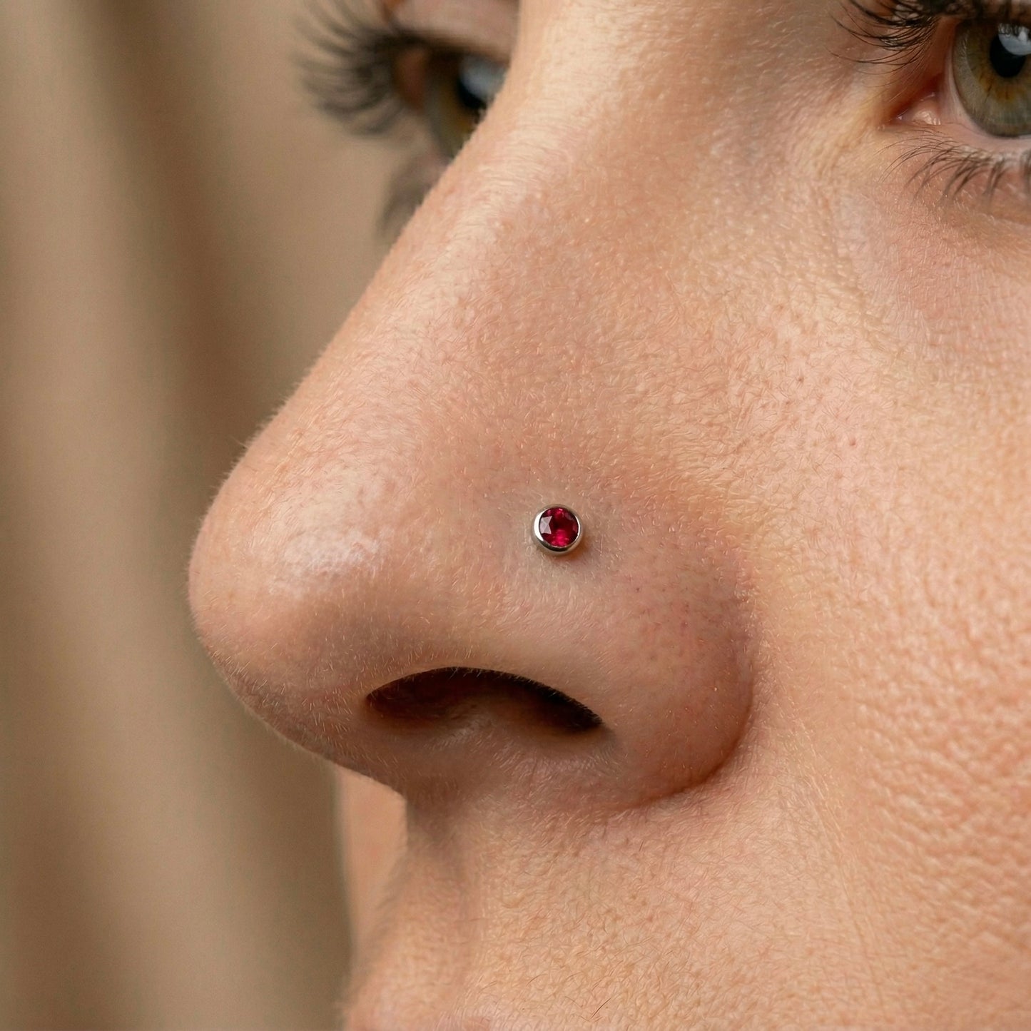 Close-up of a person's nose with a red gemstone nose piercing.