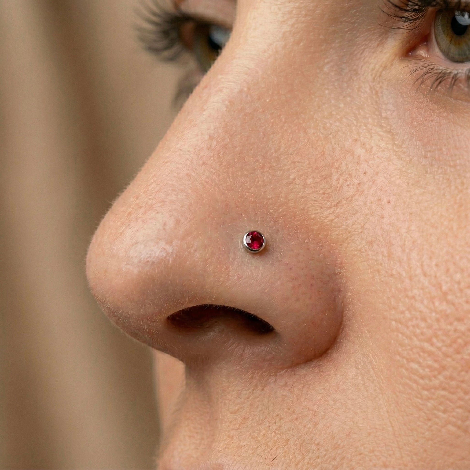 Close-up of a person's nose with a red gemstone nose piercing.