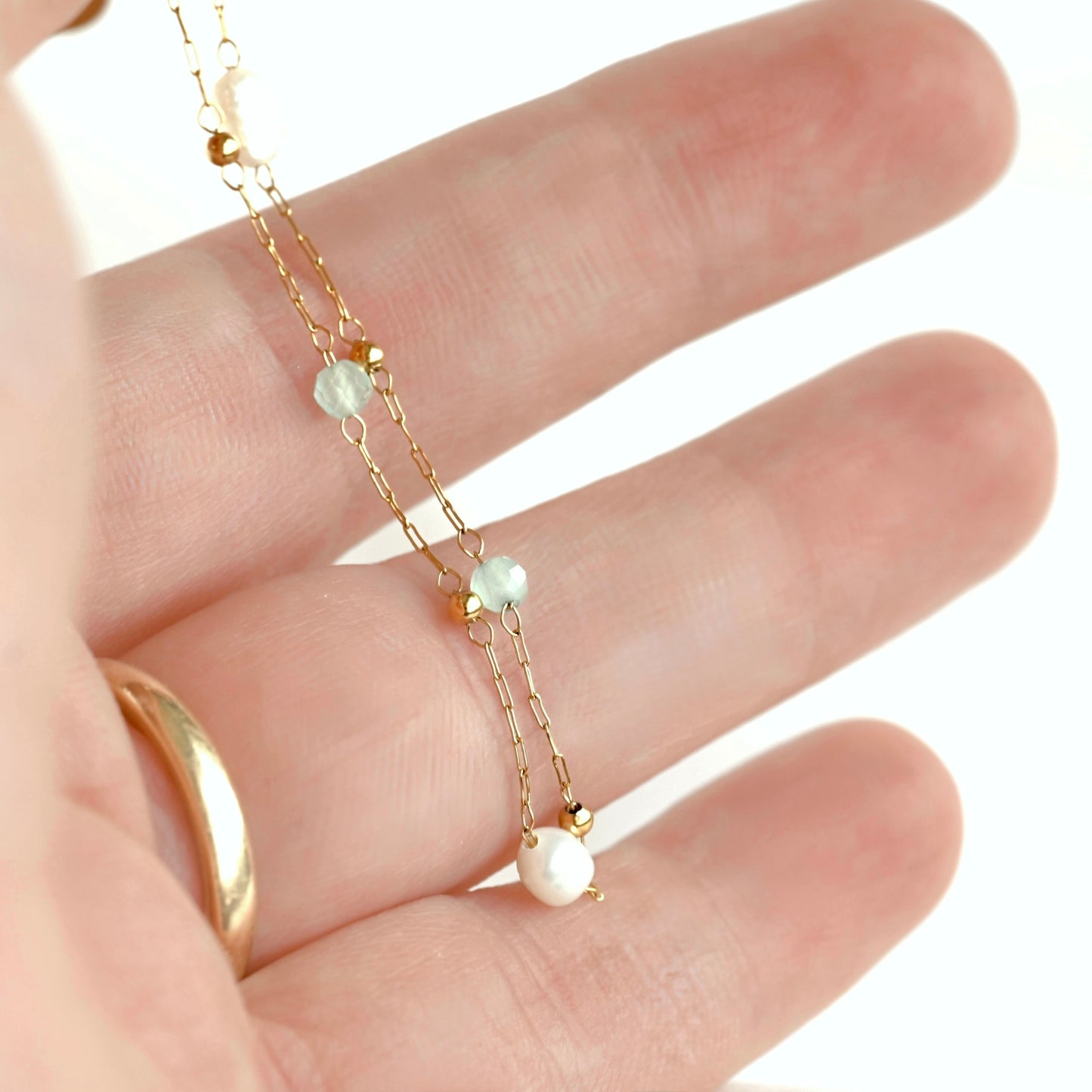 A delicate gold chain bracelet with two small white pearls tiny gold ball spacer beads and light blue plastic beads, shown draped across an open hand.