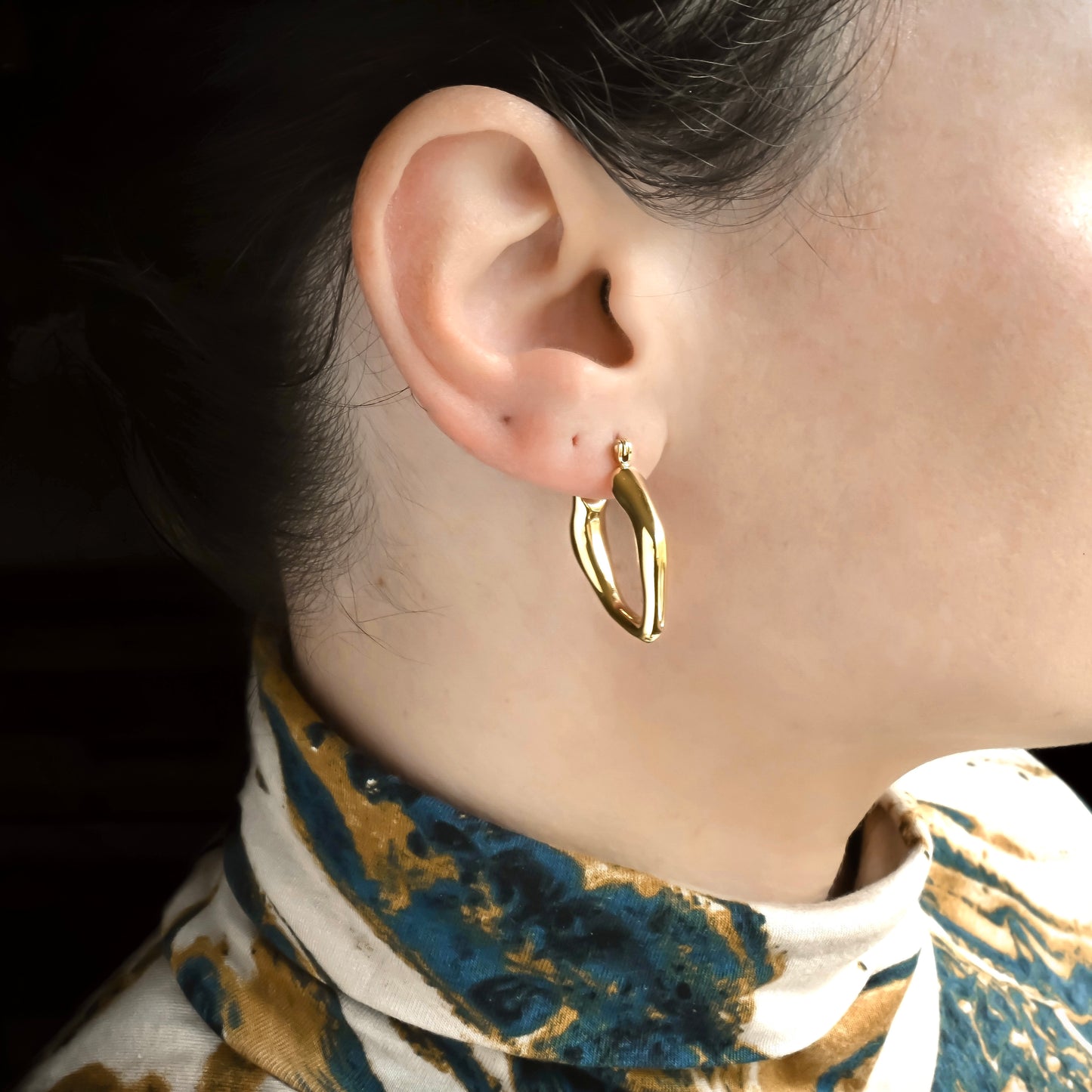 Gold V-shaped hoop earring worn by a person with a patterned garment.