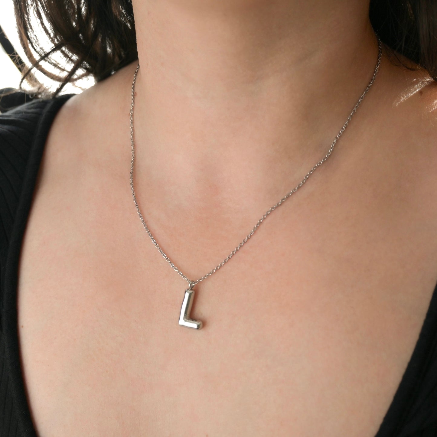 Silver necklace with a letter 'L' pendant on a person wearing a black top.