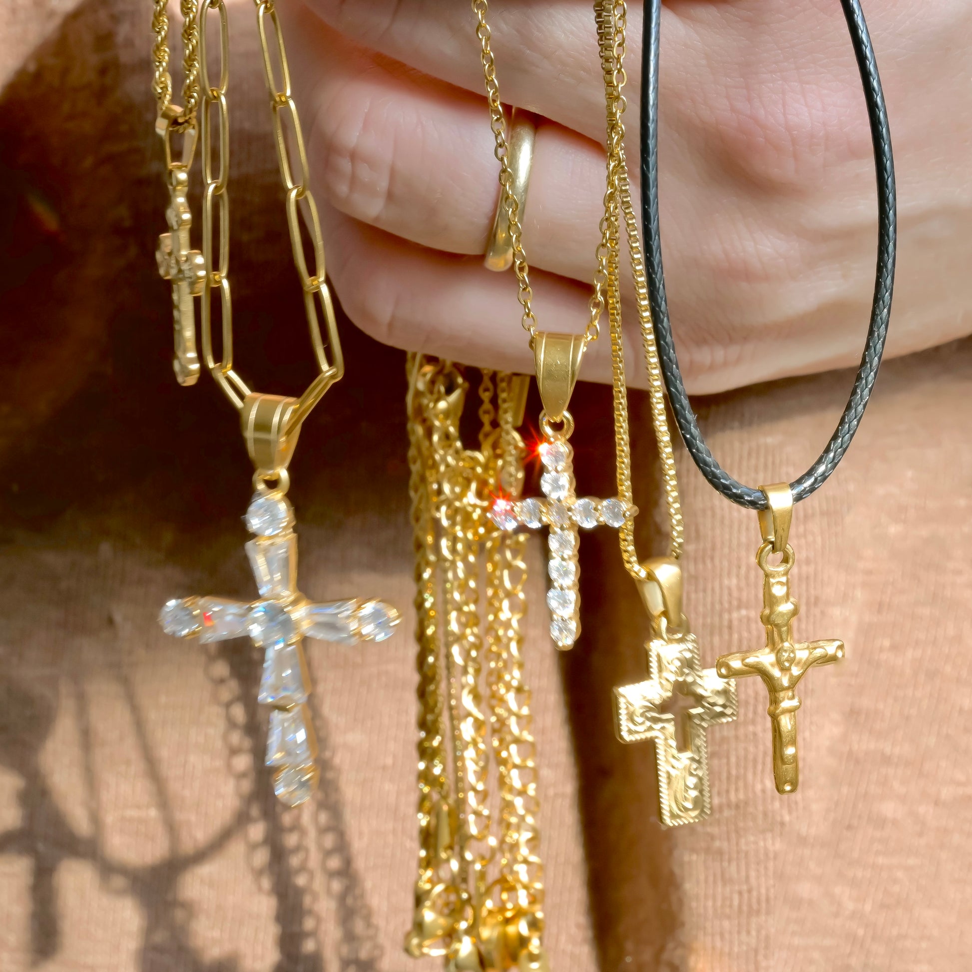 Gold cross necklaces held by a hand against a blurred background
