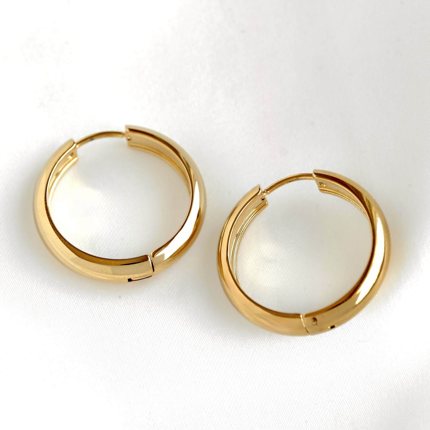 A pair of polished thick gold hoop earrings with a segmented, stepped circular design, displayed on a clean white textured surface.
