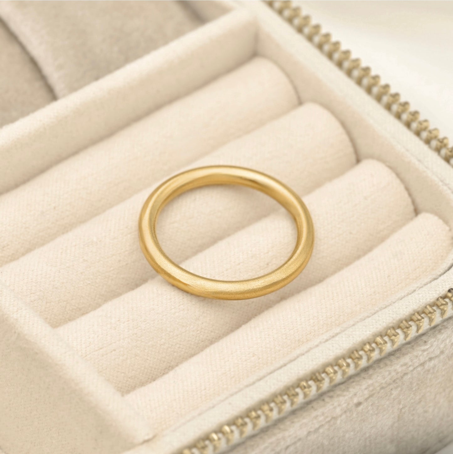 Simple gold band with grainy finish resting in beige jewelry box