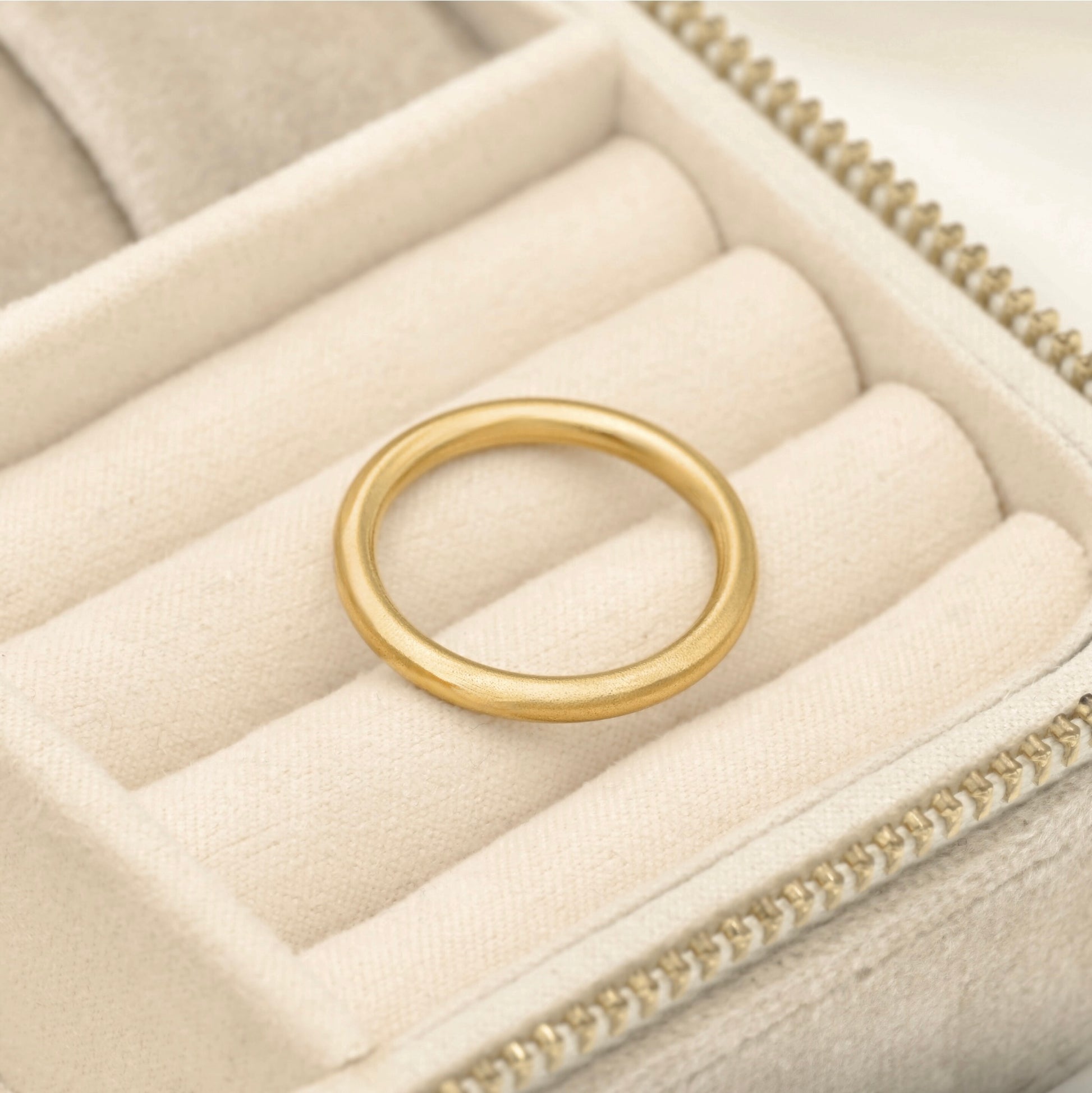 Simple gold band with grainy finish resting in beige jewelry box