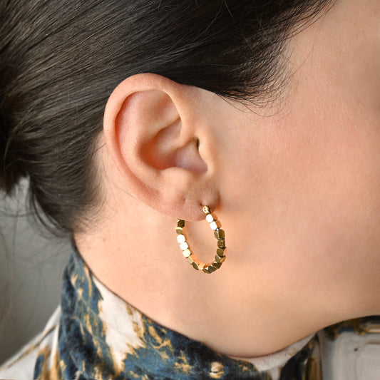 A close-up of a person's ear wearing textured gold hoop earrings with small gold bead accents.
