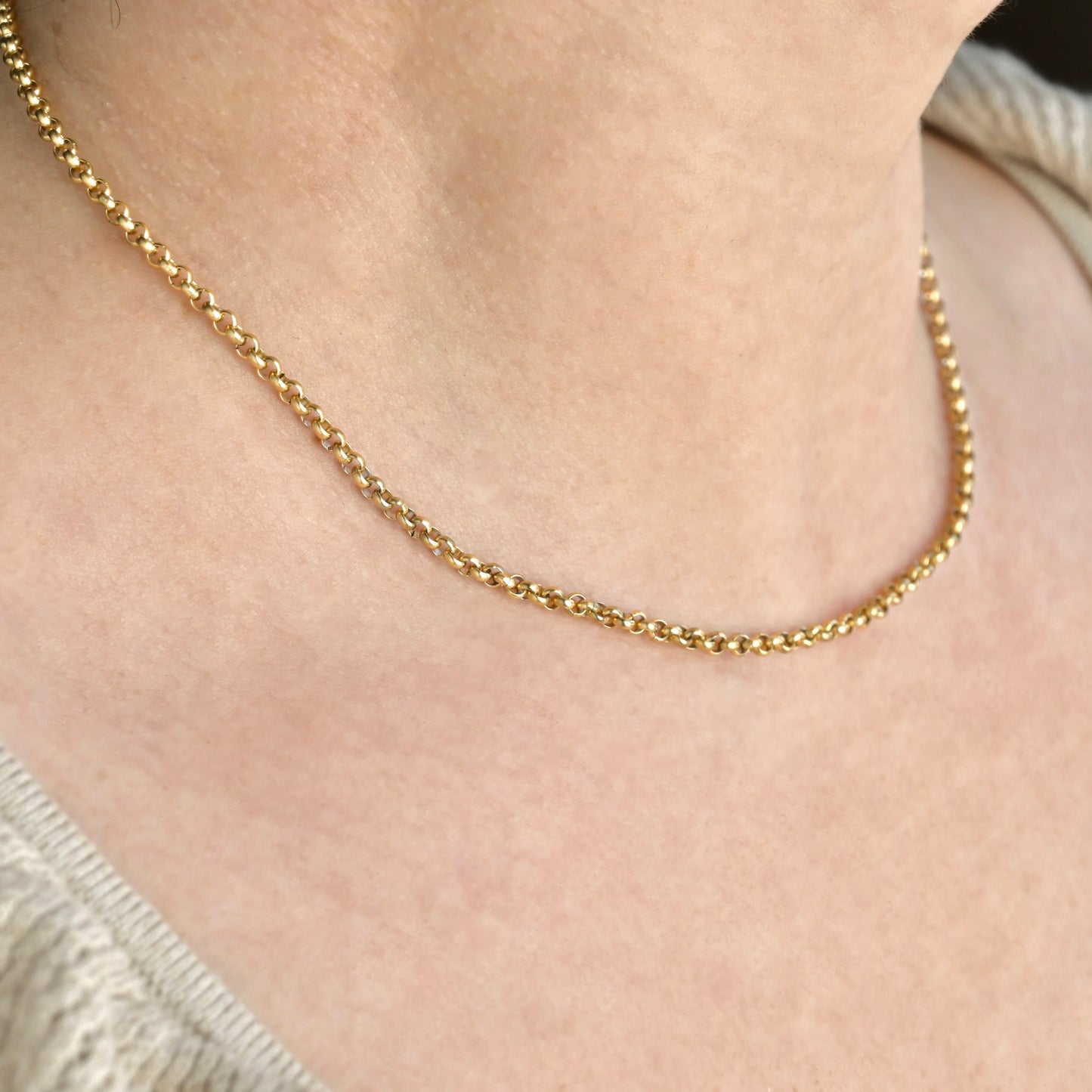 Gold necklace on a person's neck with a neutral background