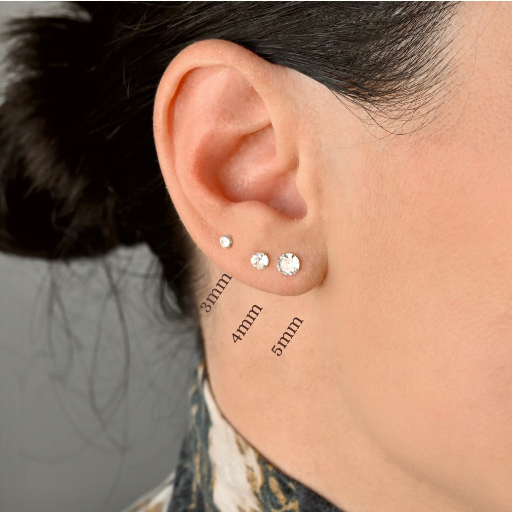 Close-up of an ear with three different sized solitaire stud earrings displayed.