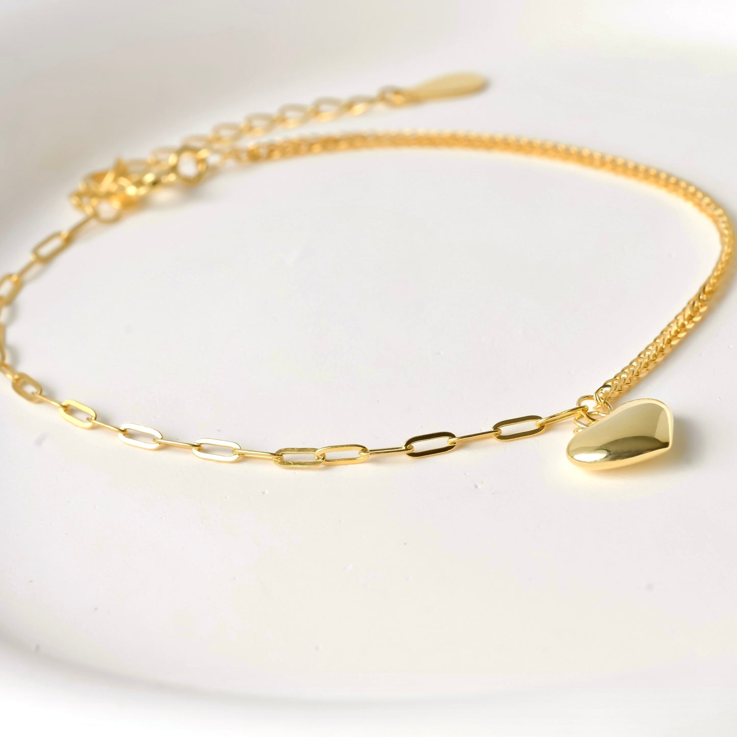 Gold bracelet with a heart pendant on a white background