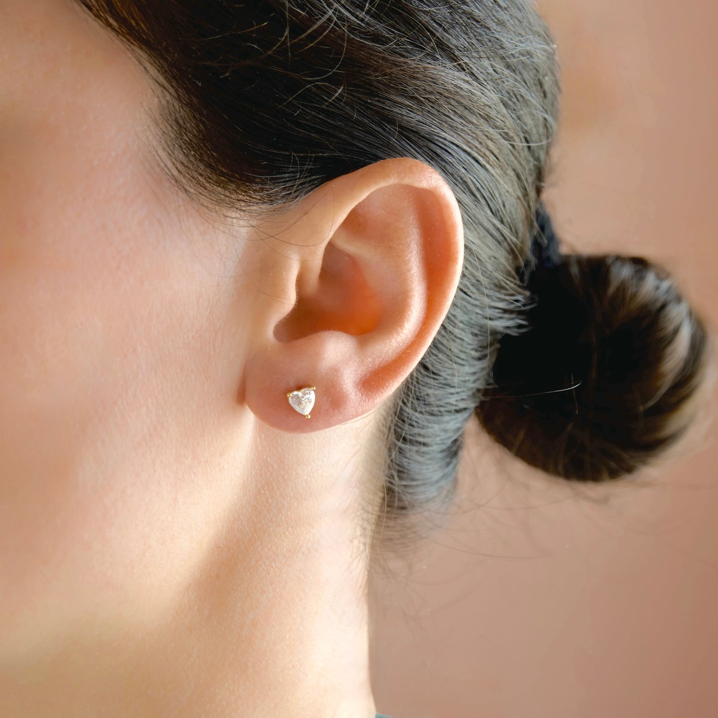 A close-up of a person's ear wearing a small heart-shaped stud earring in a silver-toned setting.