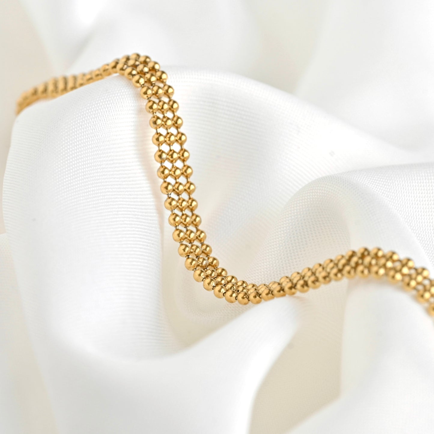 Gold beaded bracelet with 3 row beads on a white satin background