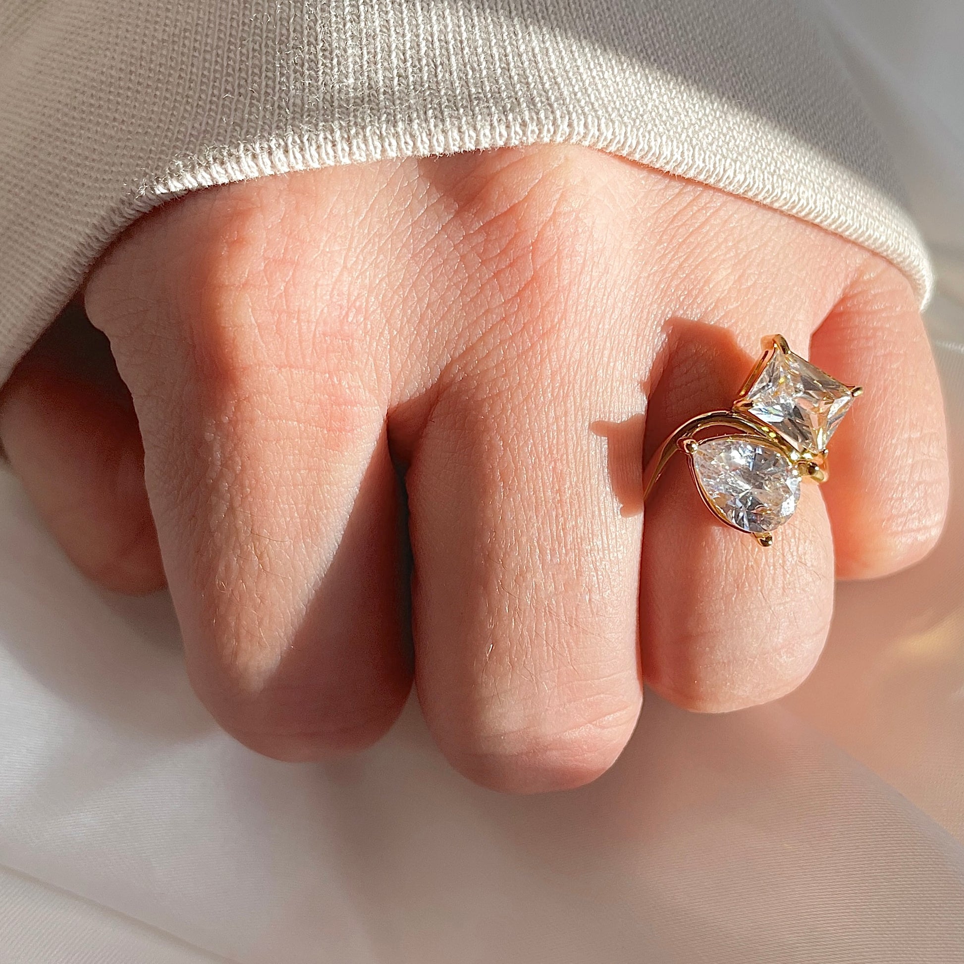 Close-up of a hand wearing a gold wave ring with two large diamonds under direct sunlight