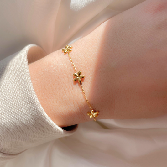 Gold bracelet with flower charms on a wrist against a neutral background