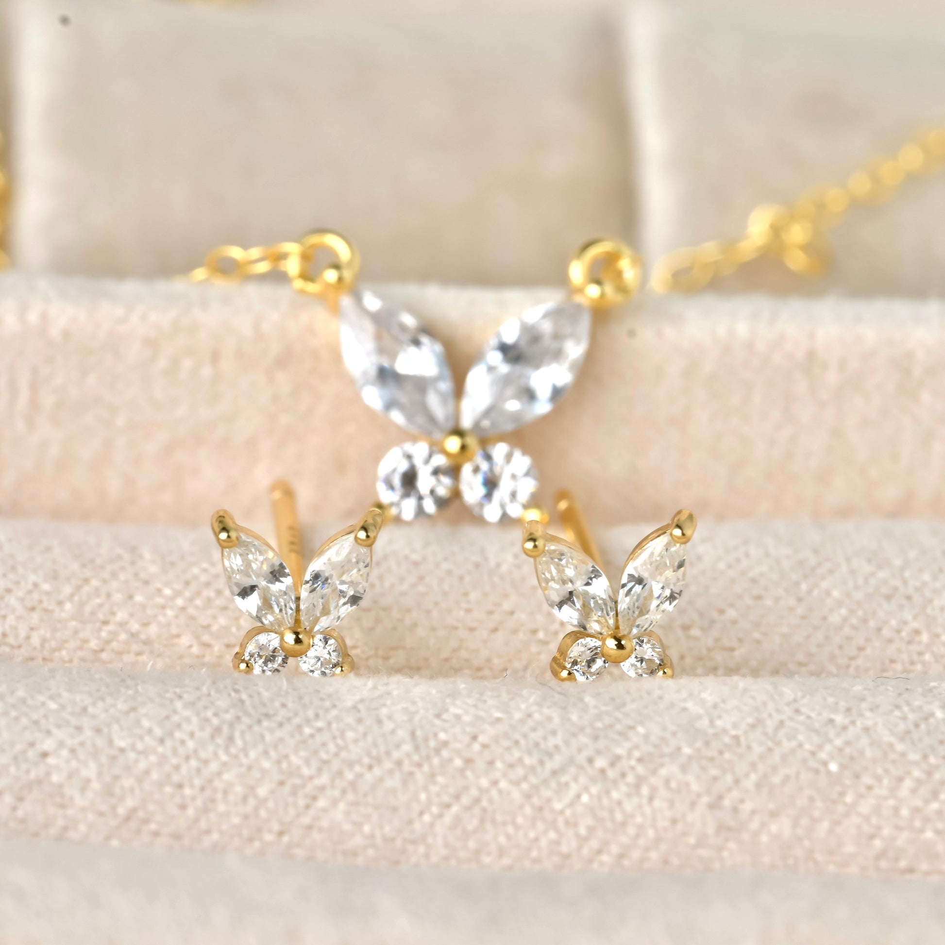 Diamond butterfly jewelry set with gold and clear stones on a beige background