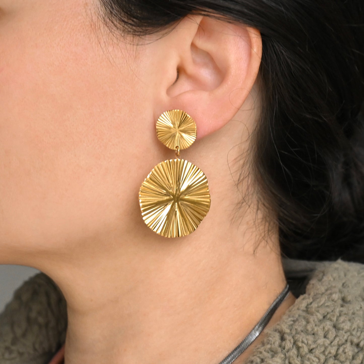 Side close-up view of oversized gold sun earrings worn by a person with dark hair.