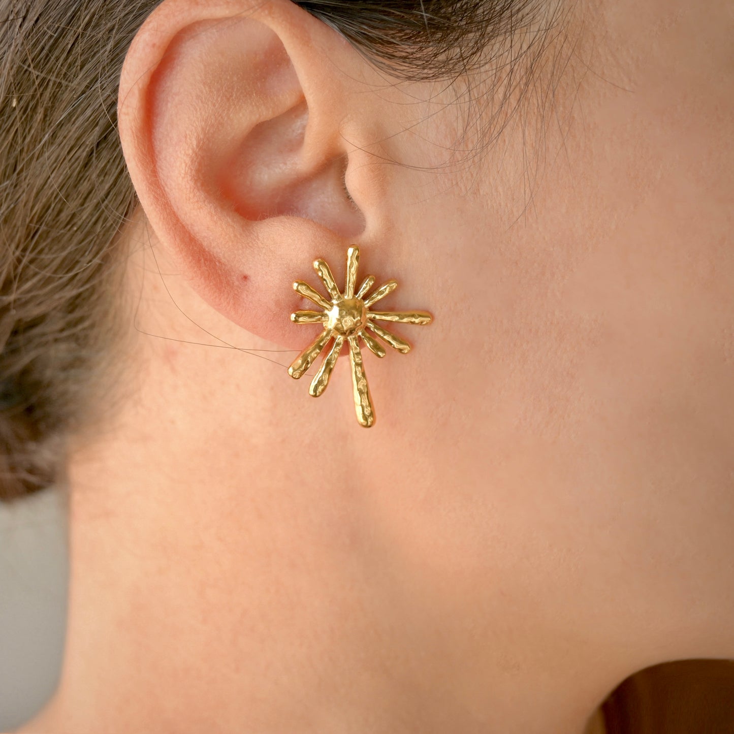 Gold sun-shaped earring worn by a person