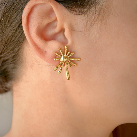 Gold sun-shaped earring worn by a person