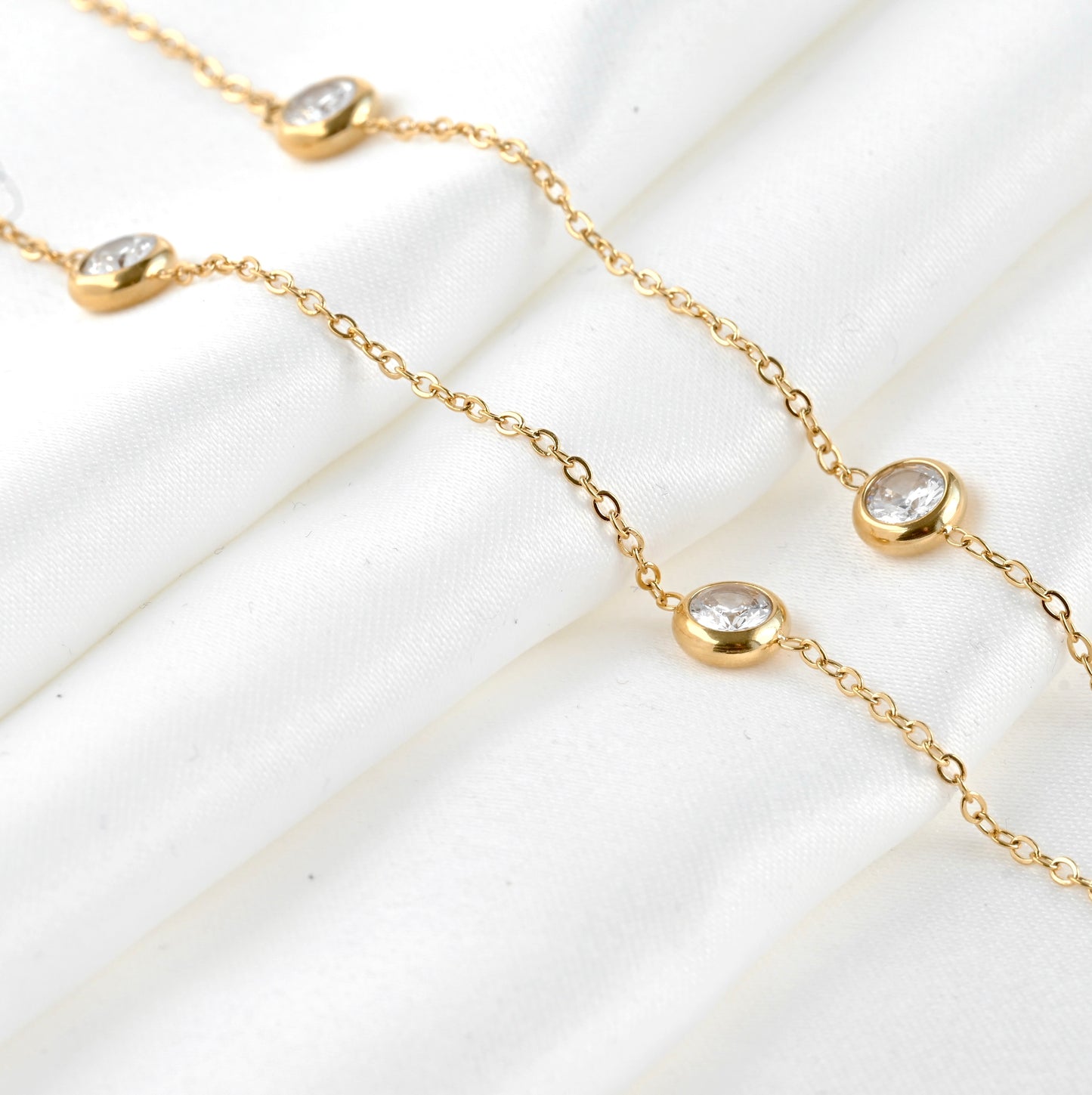 Gold necklace with small round stones on a white satin fabric
