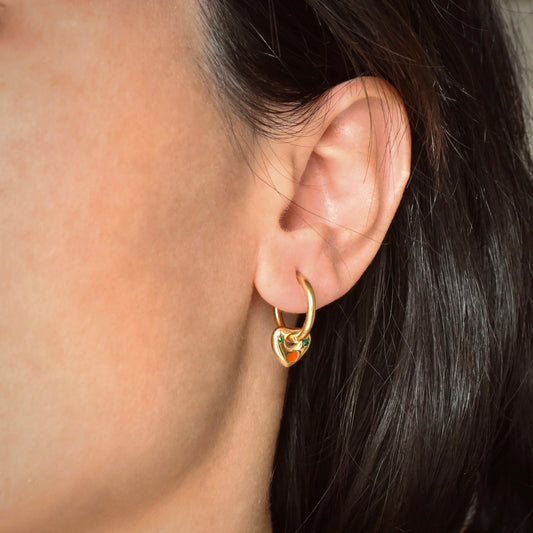 Gold heart-shaped hoop earring worn by a person with dark hair.