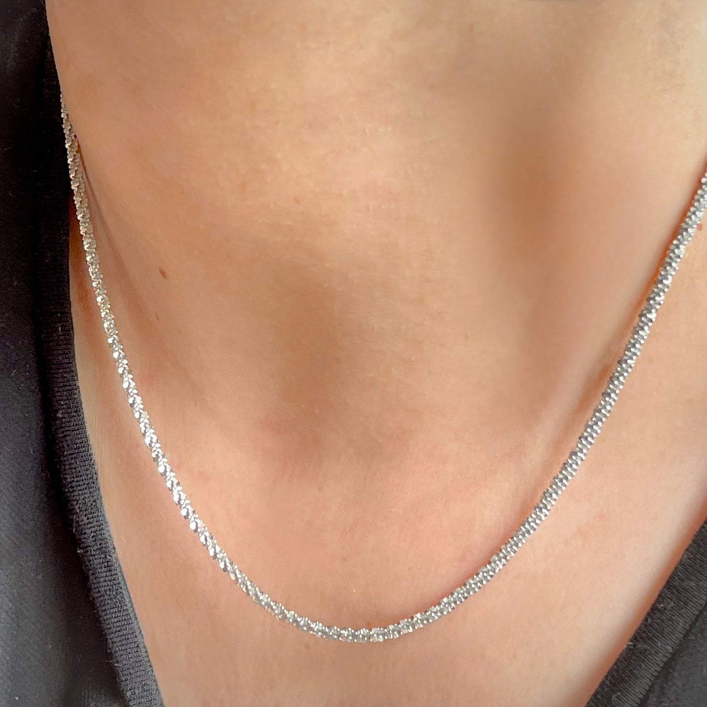 Silver rope chain necklace on a person's neck with a neutral background
