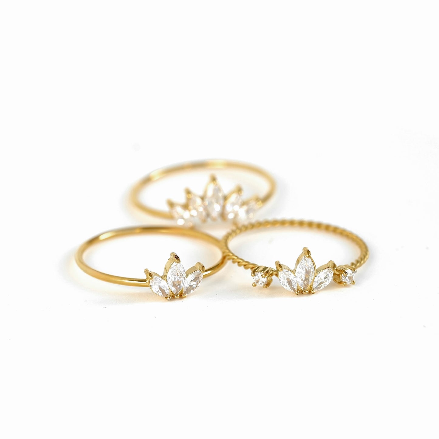 Three gold rings with clear marquise-cut gemstones arranged on a white background.