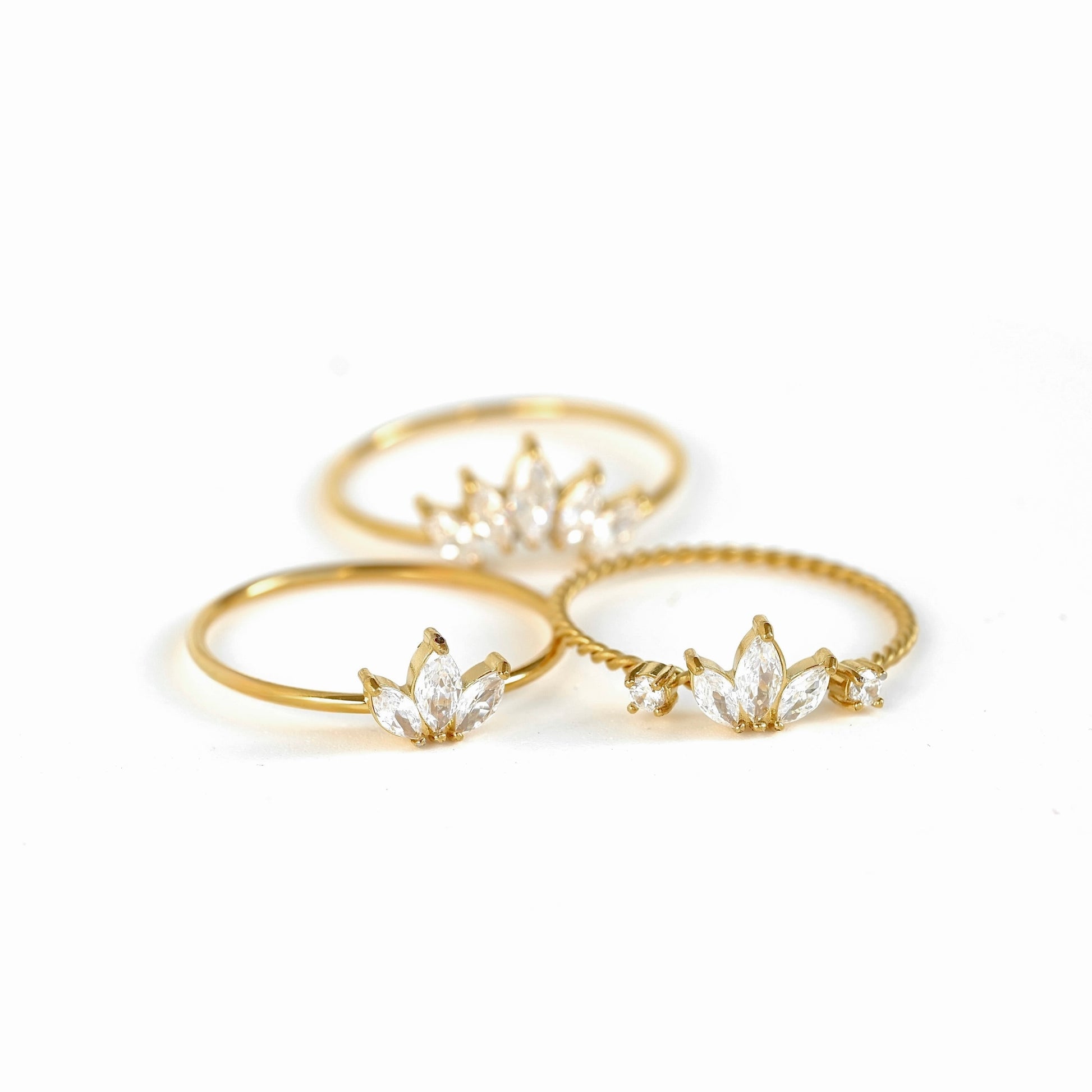 Three gold rings with clear marquise-cut gemstones arranged on a white background.