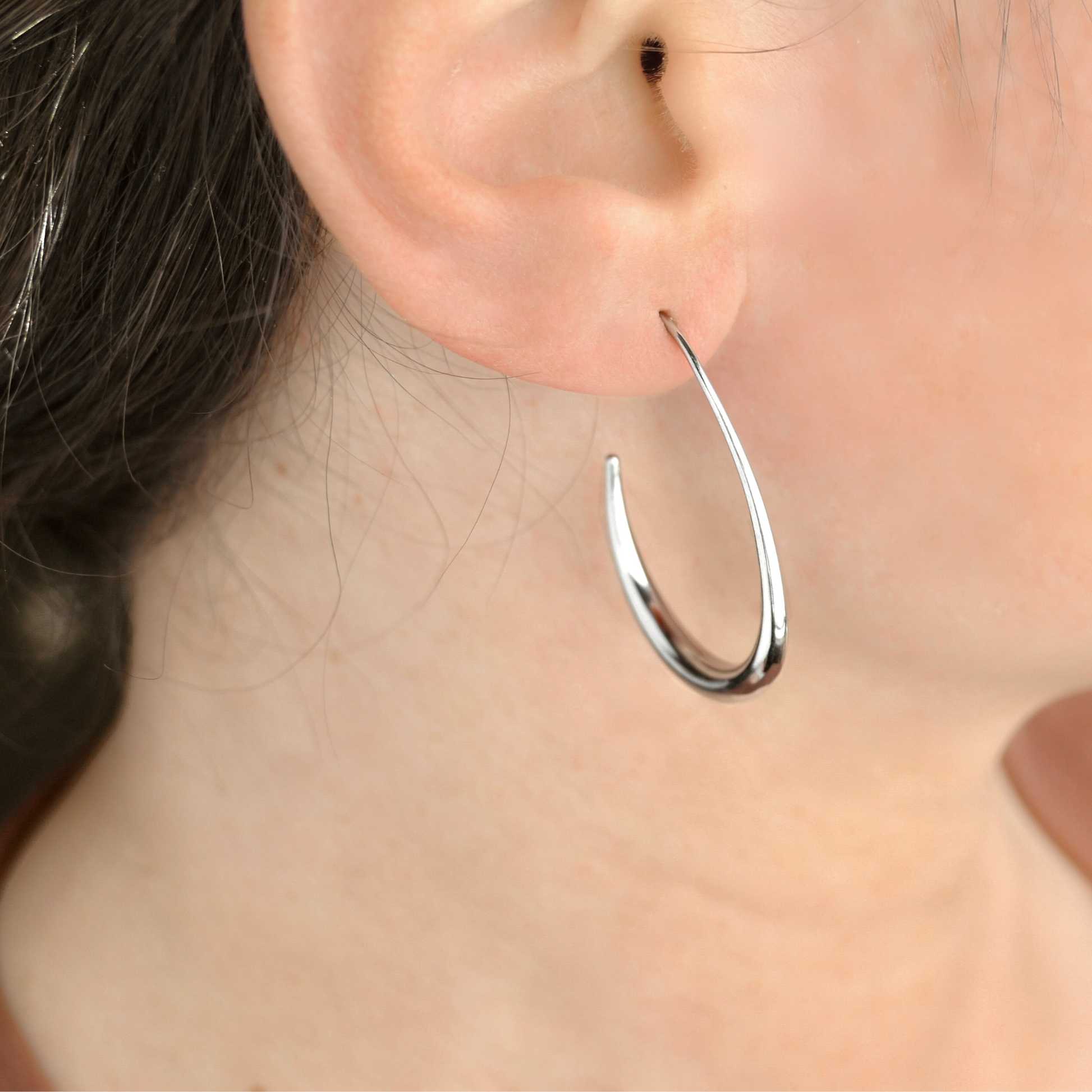 Silver pear-shaped  earring worn by a person with blurred background