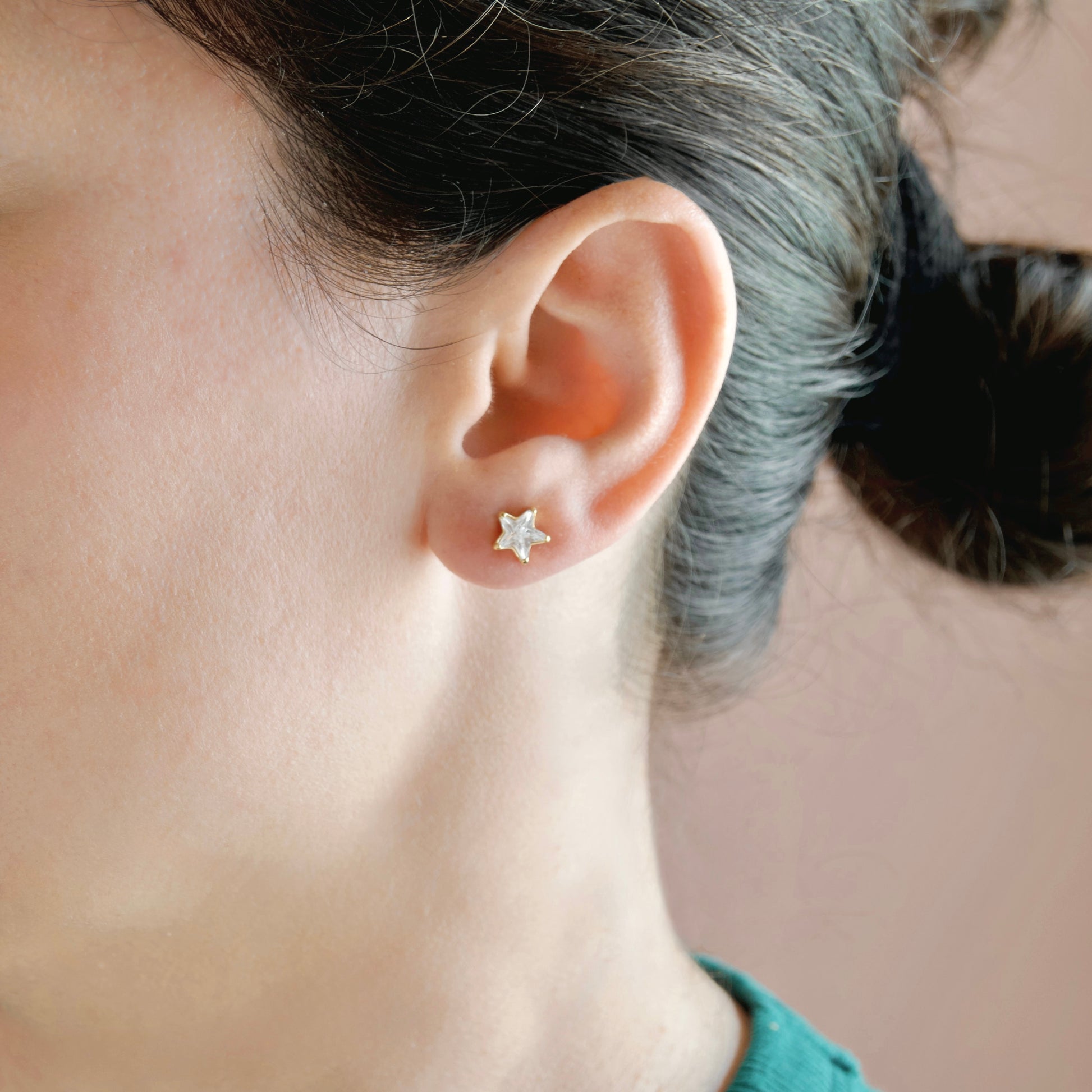 A close-up of a person's ear wearing a small gold star-shaped stud earring against a soft beige background.