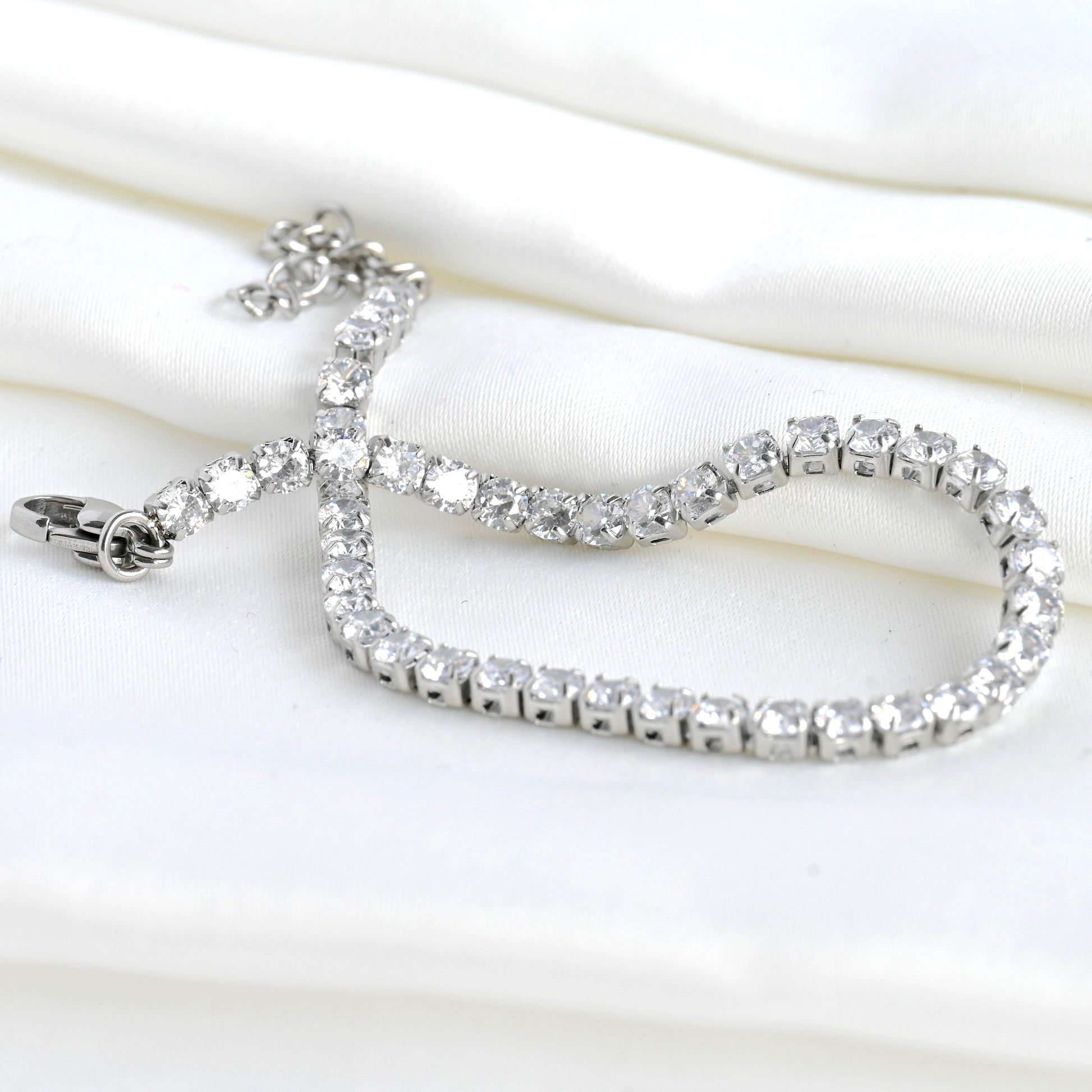 Close up view of silver bracelet with clear CZ, a lobster claw clasp and extender chain on a white background