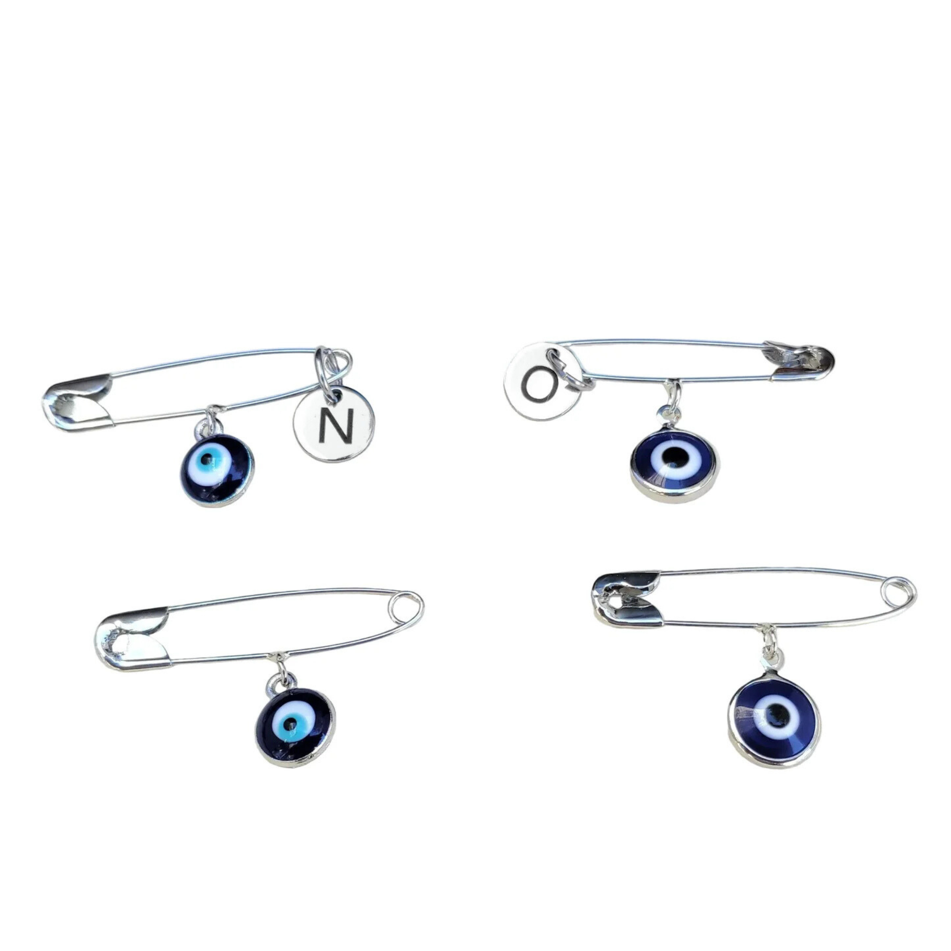 Set of four silver safety pins with evil eye charms  and initial discs on a white background