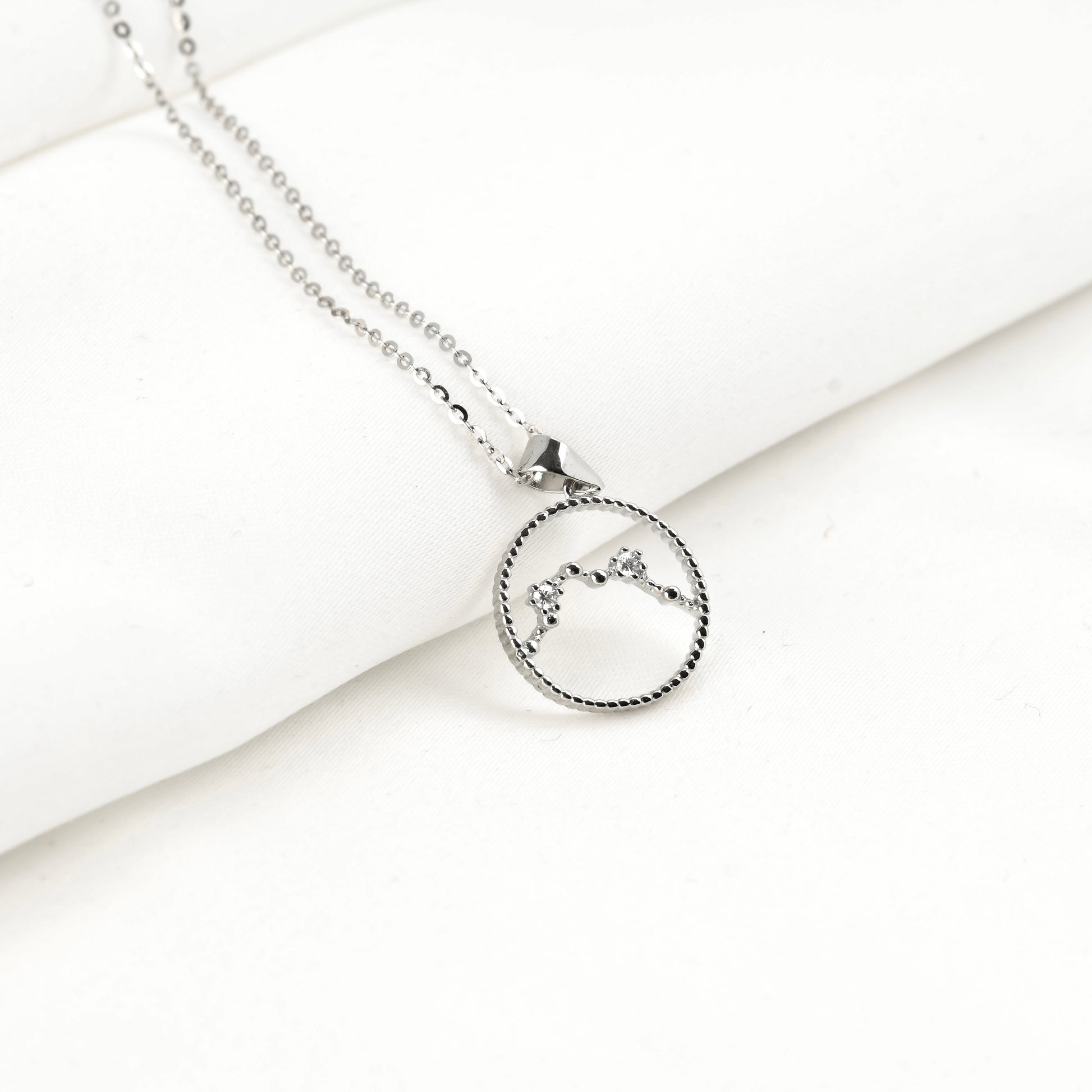 Silver necklace with a circular constellation pendant on a white surface