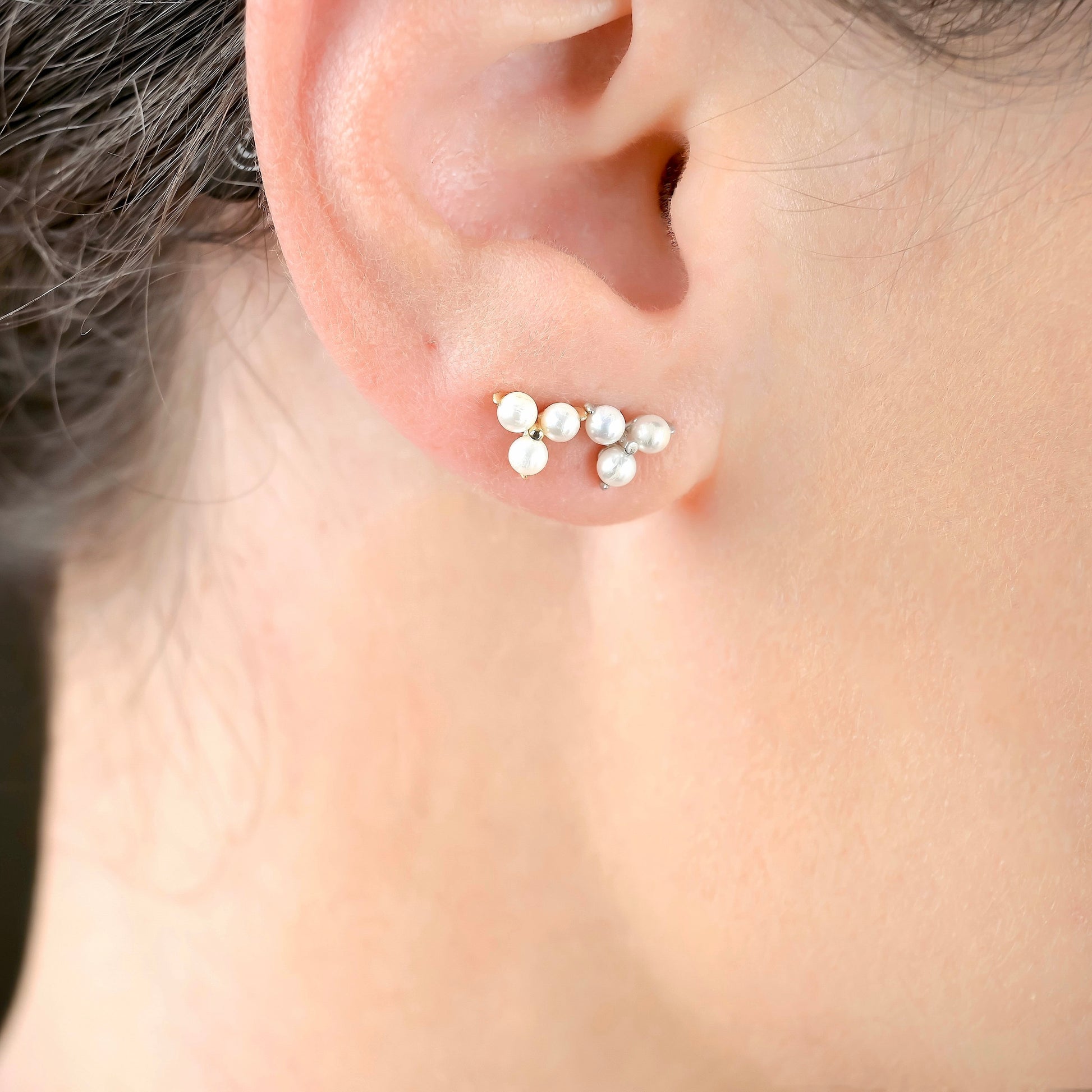 Close-up of an ear wearing a silver and gold 3-leaf clover stud earrings with pearls accents