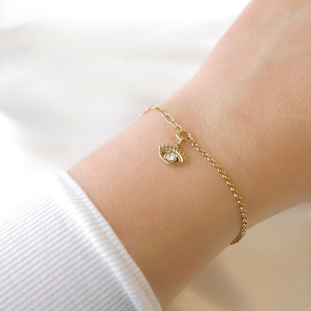 A delicate gold chain bracelet with an evil eye charm featuring a clear crystal, shown worn on a person's wrist.