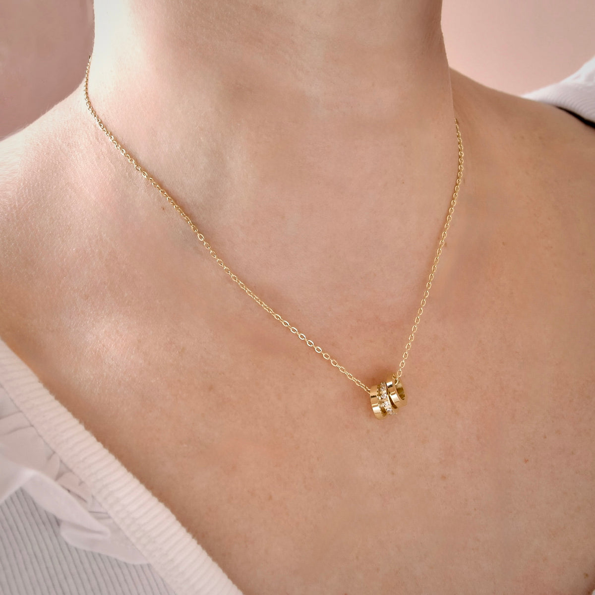 A delicate gold chain necklace with a small cluster of three gold rings pendant, shown worn on a model's neck.