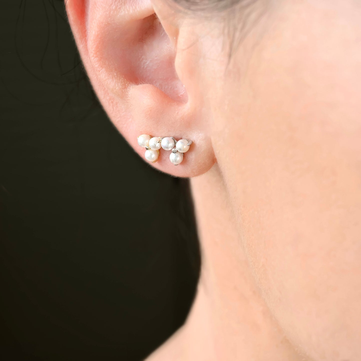 Gold and silver pearl stud earrings worn by a person against a neutral background