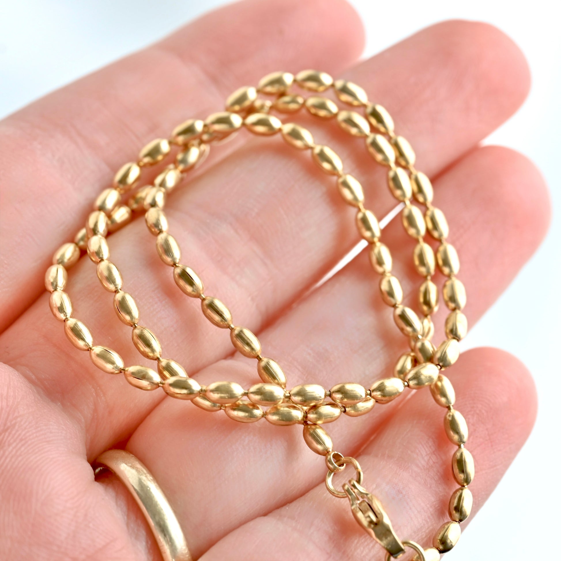 A gold chain necklace with a textured, polished oval link design, draped over a person's hand against a white background.