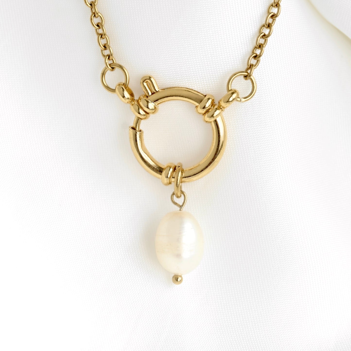 Gold chain necklace with a toggle ring clasp and a dangling baroque pearl pendant, displayed on a white fabric surface.