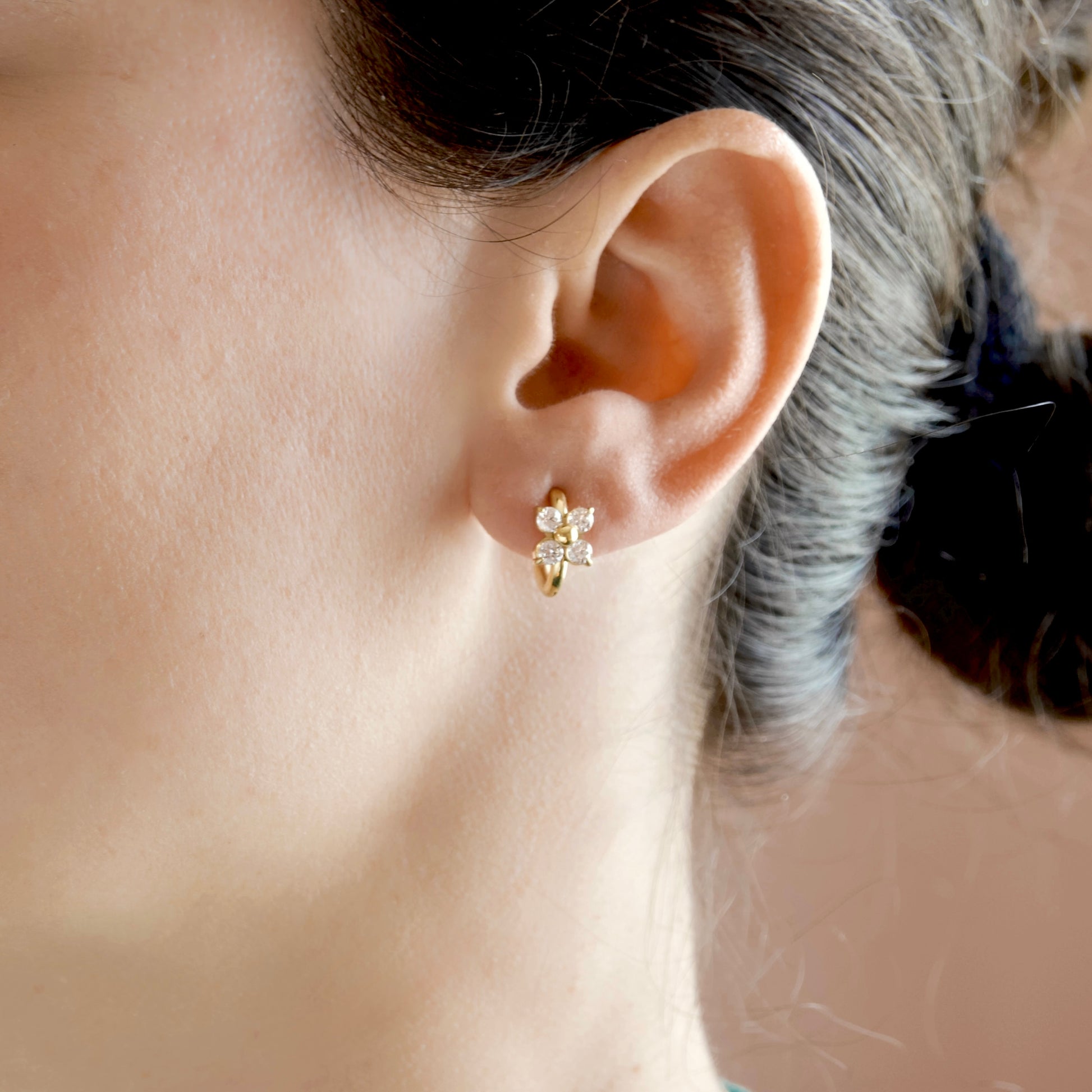 A close-up of a person's ear wearing a small gold huggie hoop earring adorned with clear crystals.