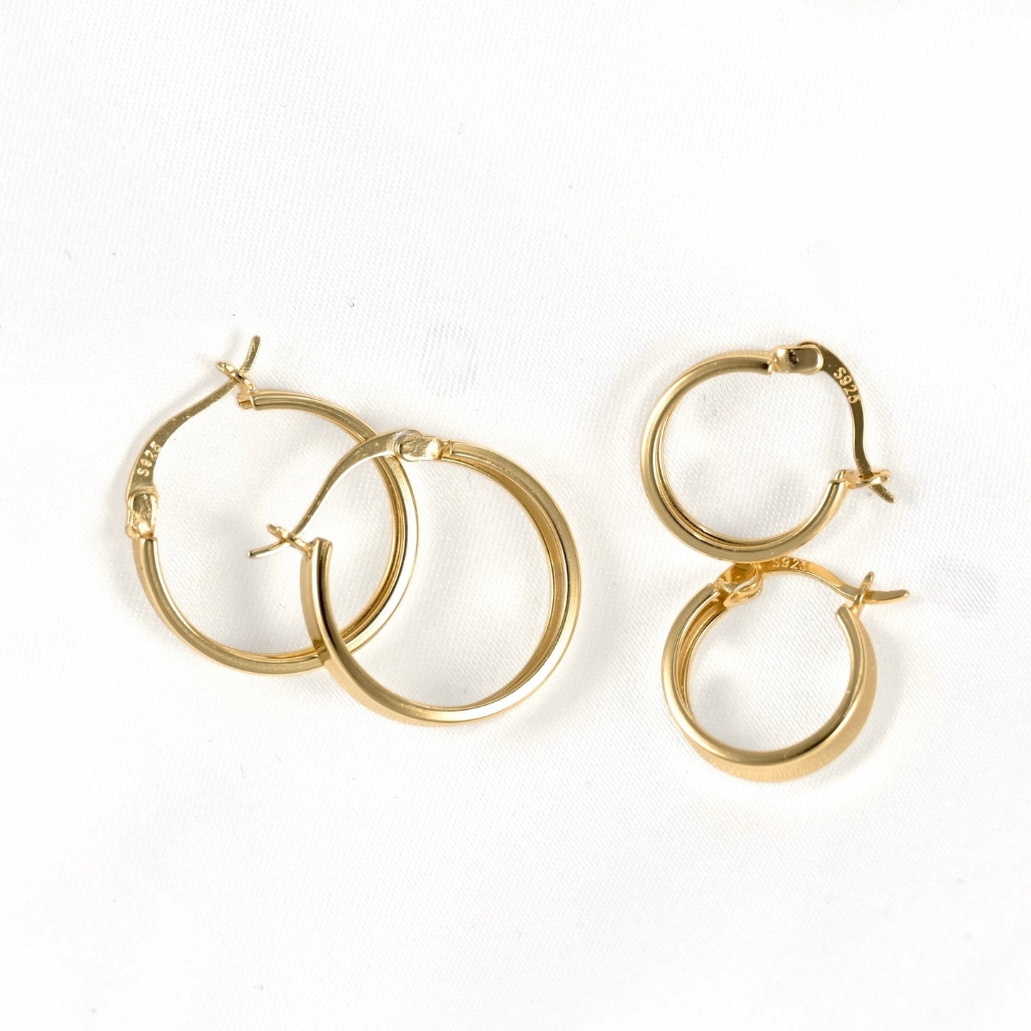 Four gold hoop earrings of varying sizes arranged on a plain white background.