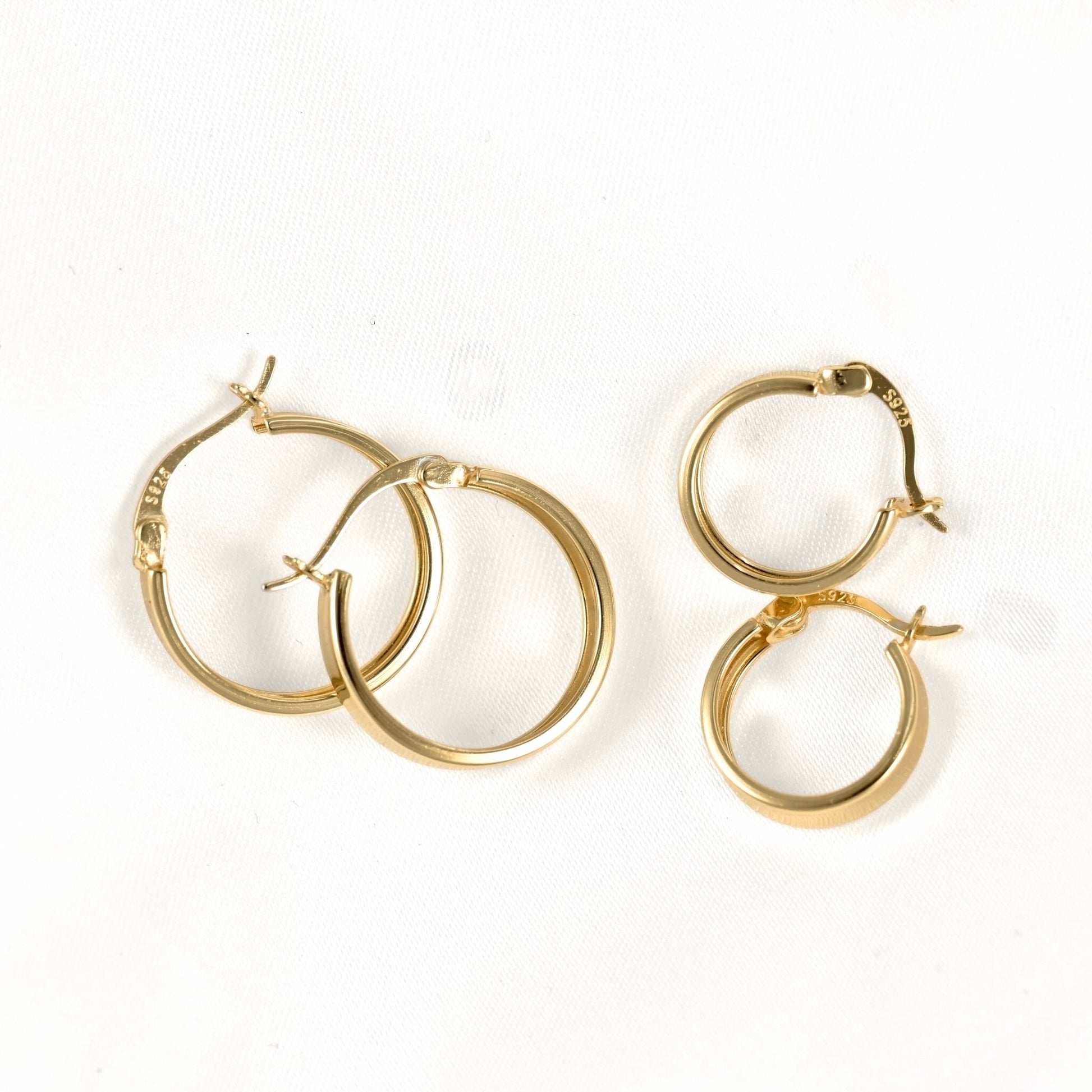 Four gold hoop earrings of varying sizes arranged on a plain white background.