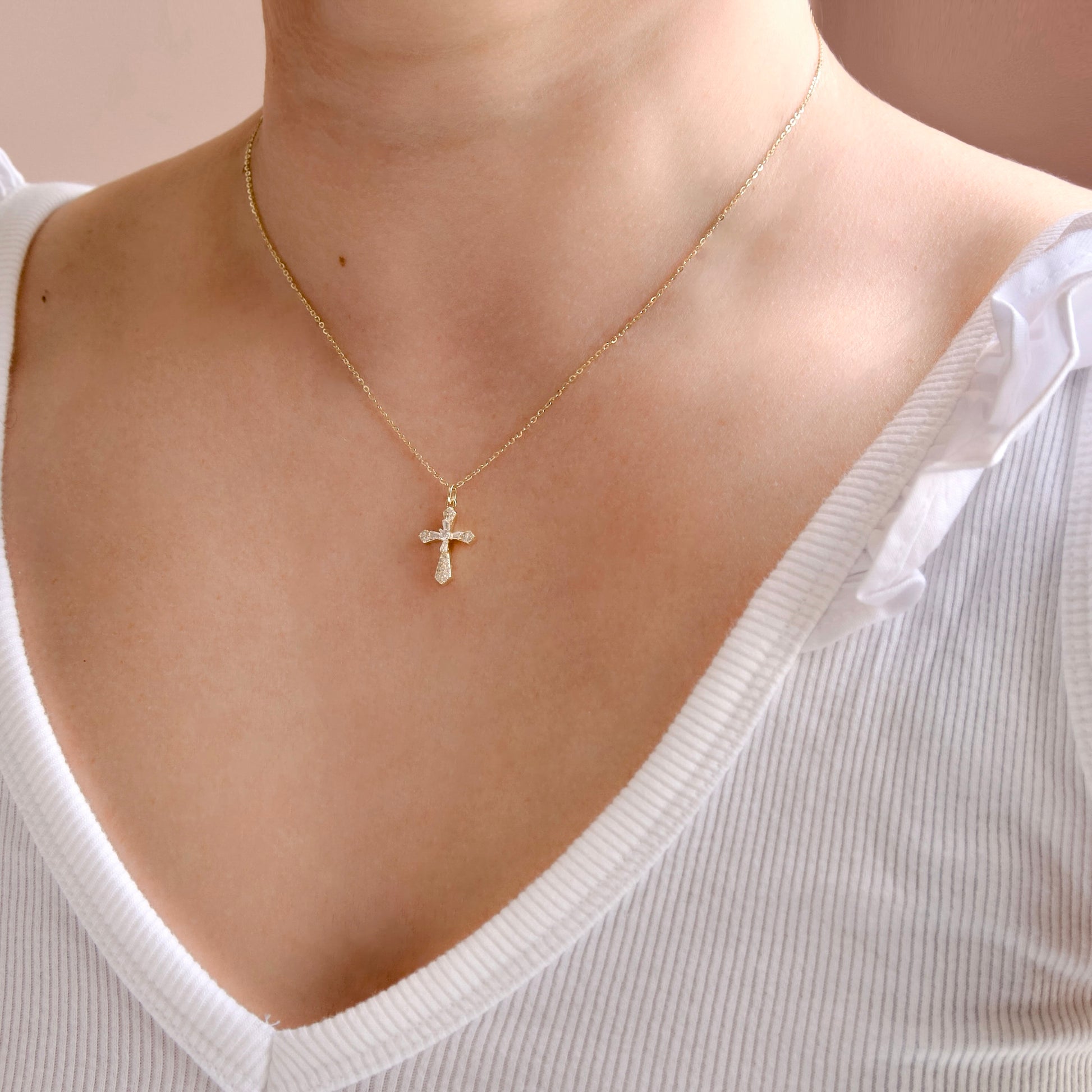 Gold necklace with a diamond cross pendant worn by a person in a white top.