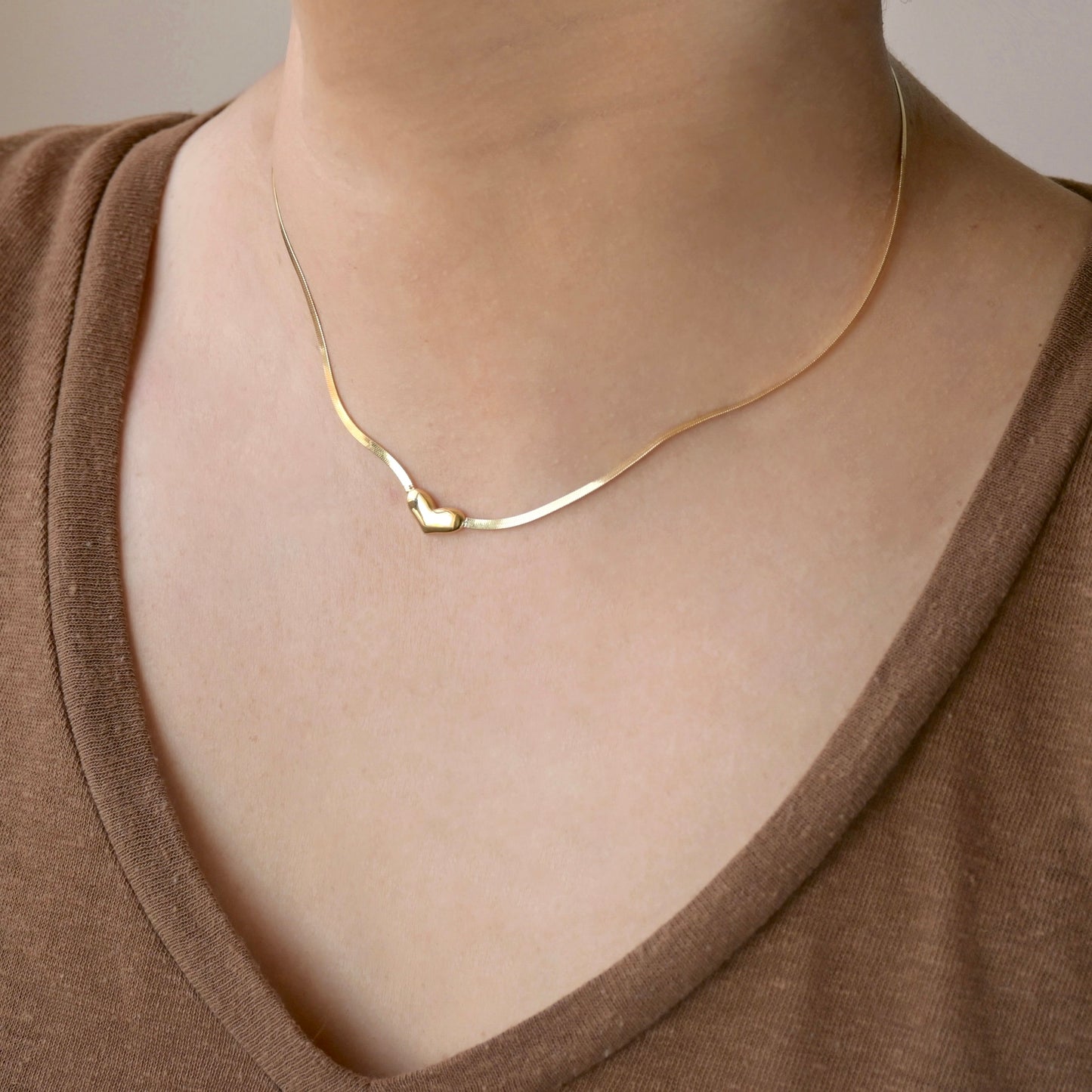 Gold heart necklace on a person wearing a brown top